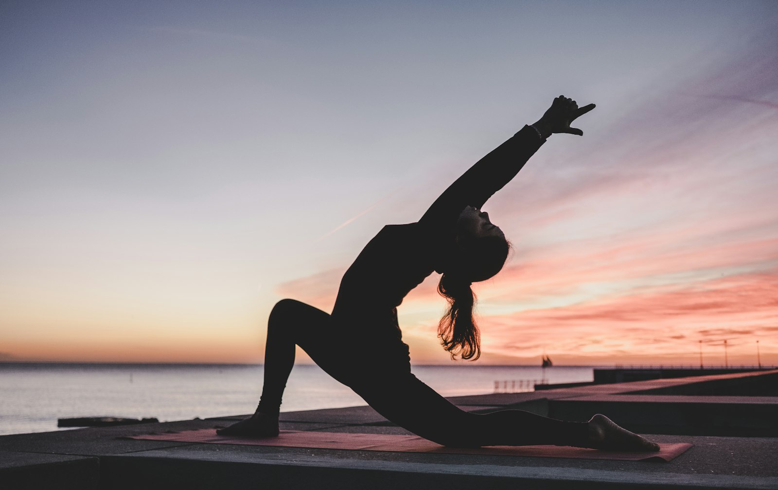 Siluetă practicând yoga la răsărit, pe malul mării